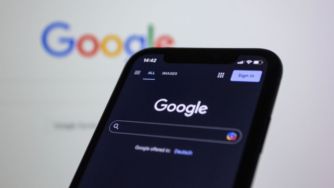 services-01 Smartphone screen showing Google search in dark mode with the Google logo in the background.